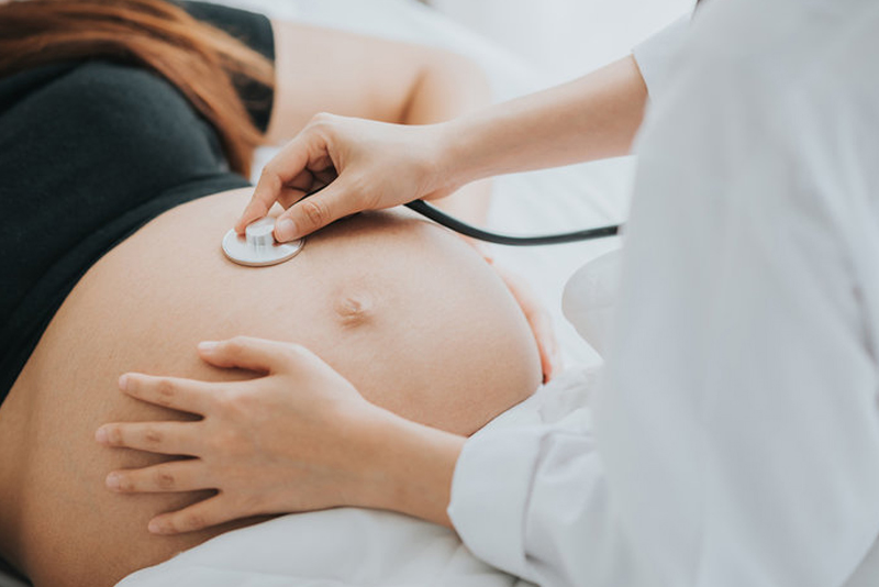 Healthcare provider placing a stethoscope on a pregnant woman’s abdomen during an examination.